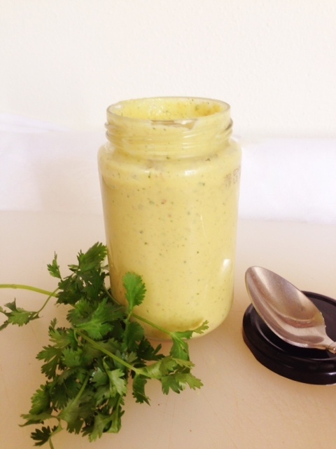 Delectable "Yumm" Sauce in a mason jar next to sprigs of parsley on a white table.