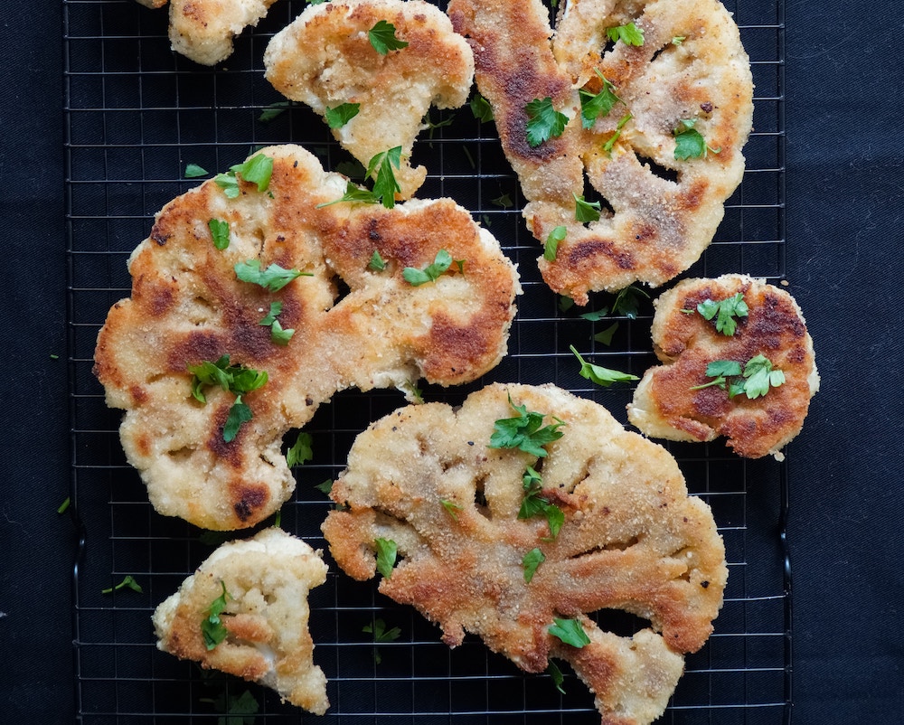 cauliflower steak pieces on a wire rack on a black background