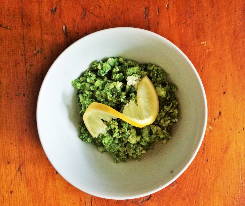 Vegan Spirulina Cauliflower garnished with a lemon slice, in a white bowl, on a wooden table.