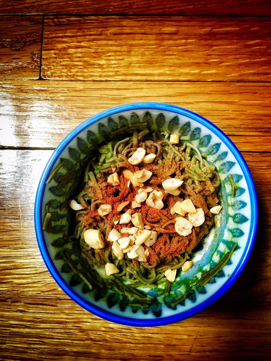 Vegan matcha soba noodles in a blue patterned bowl against a wooden table