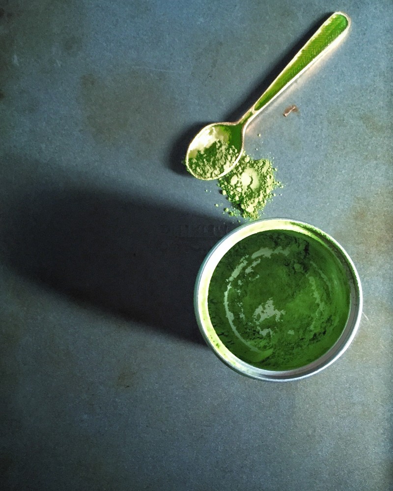 a little bowl of green matcha powder on a table. A spoon is lying next to it.
