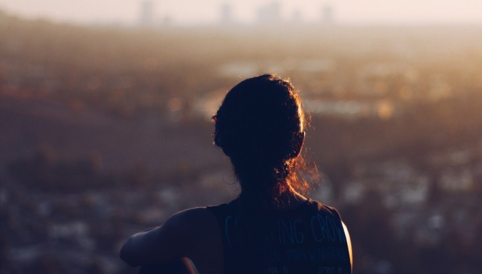 A silhouette of a woman looking out at the cityscape around twilight, contemplating whether she should quit her job.