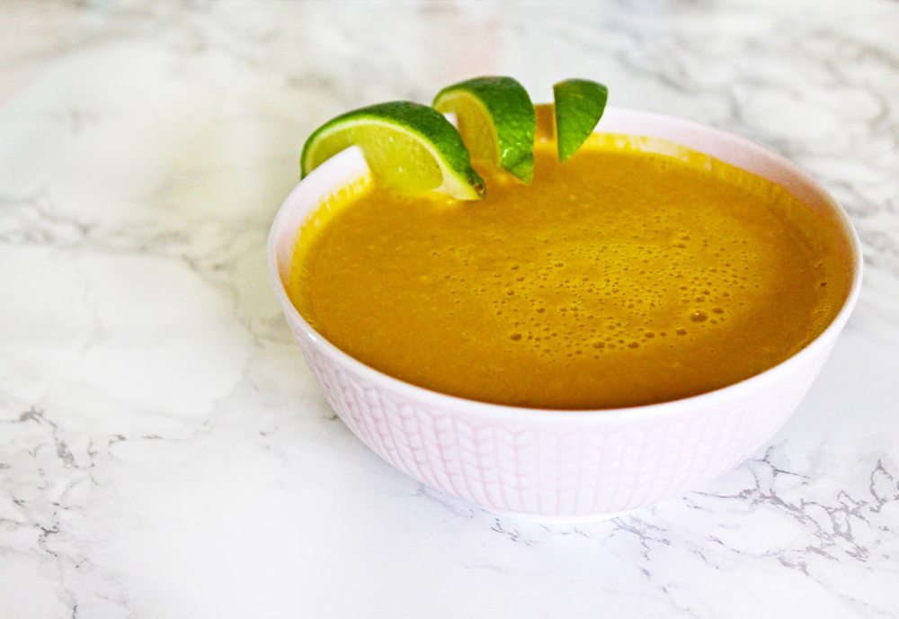 cropped view of lime coconut carrot soup in a white bowl, garnished with lime wedges and on a marble tabletop