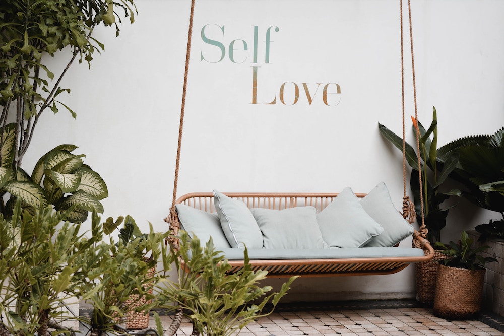 a bench surrounded by plants. On the wall behind the bench, "self-love" is written. 