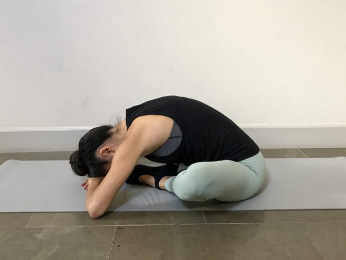 5 Best Stretches To Achieve The Middle Splits. A young woman wearing a tank top and yoga pants is doing a butterfly foldover stretch for the hip flexors. 