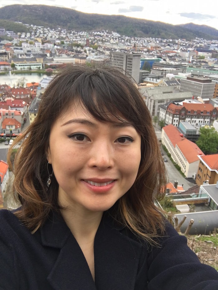How I Got Rid Of My Life-Long Under-Eye Bags: a woman, aged 30, is standing on top of a hill in Bergen, Norway, smiling at the camera. Her under-eye bags are clearly visible.