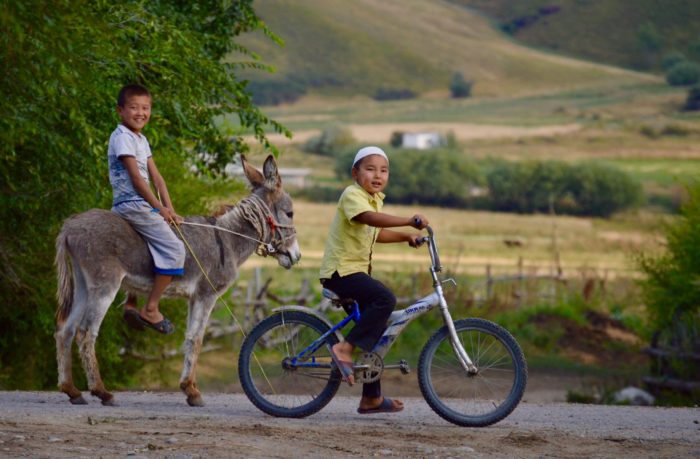 children in Kyrgzstan riding a donkey and a bike