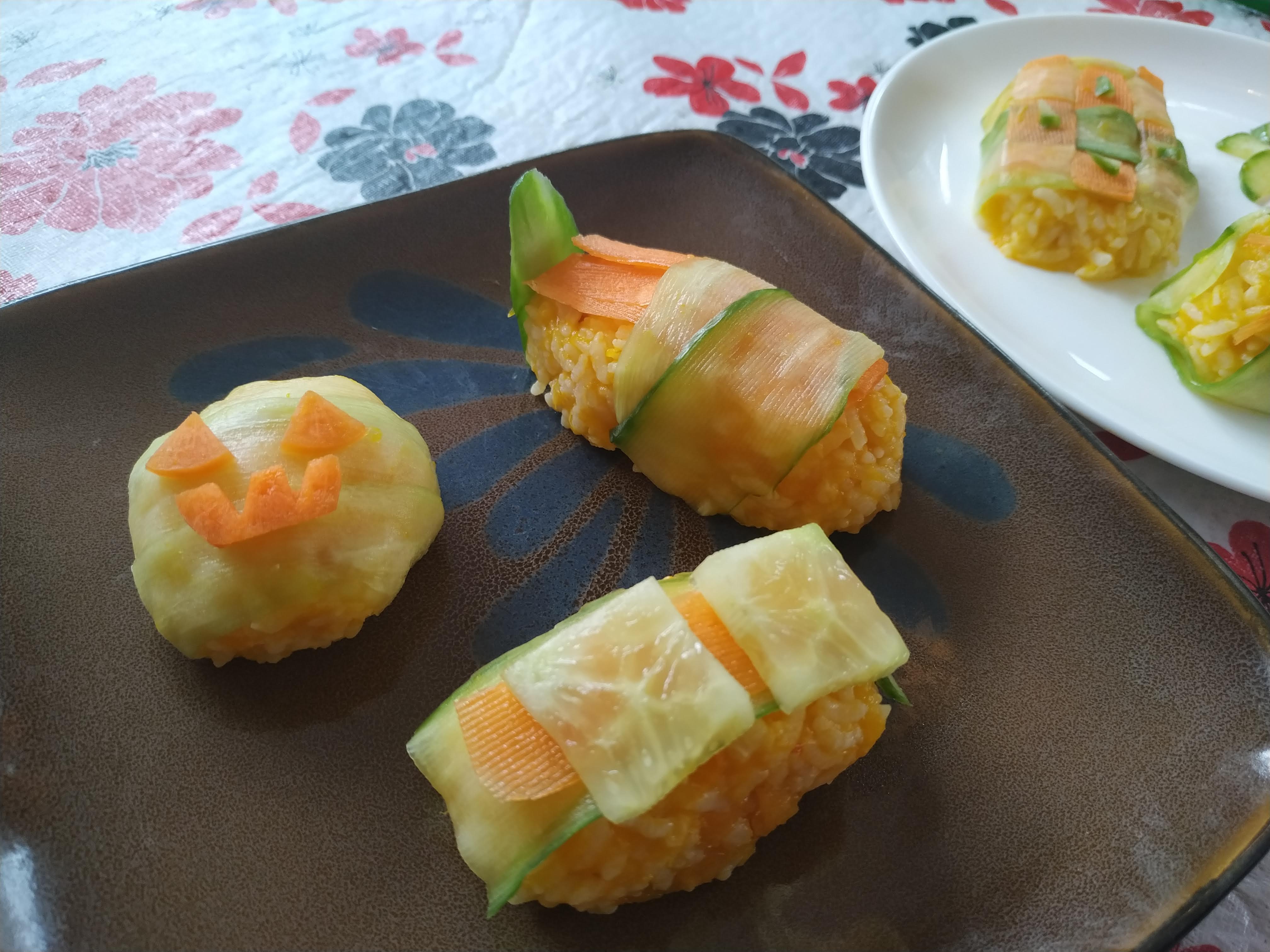 A plate of halloween themed sushi with pumpkin, carrot, rice, and cucumber