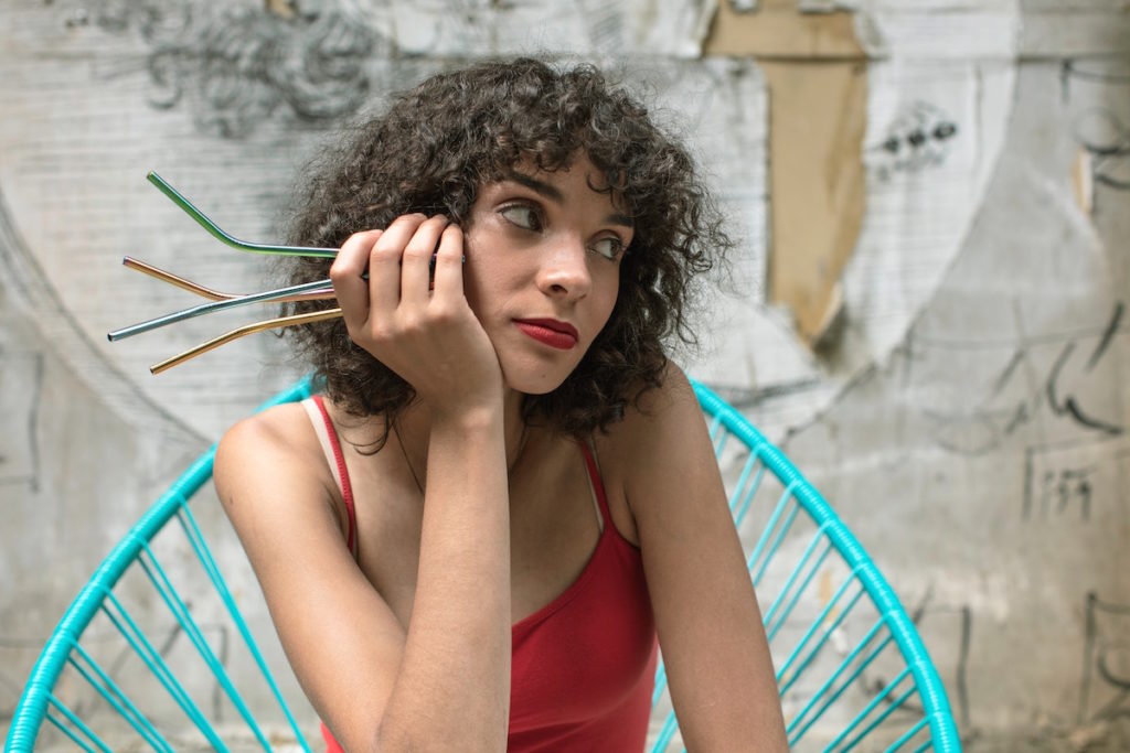 a curly haired woman looks introspective while holding metal straws in her hand.