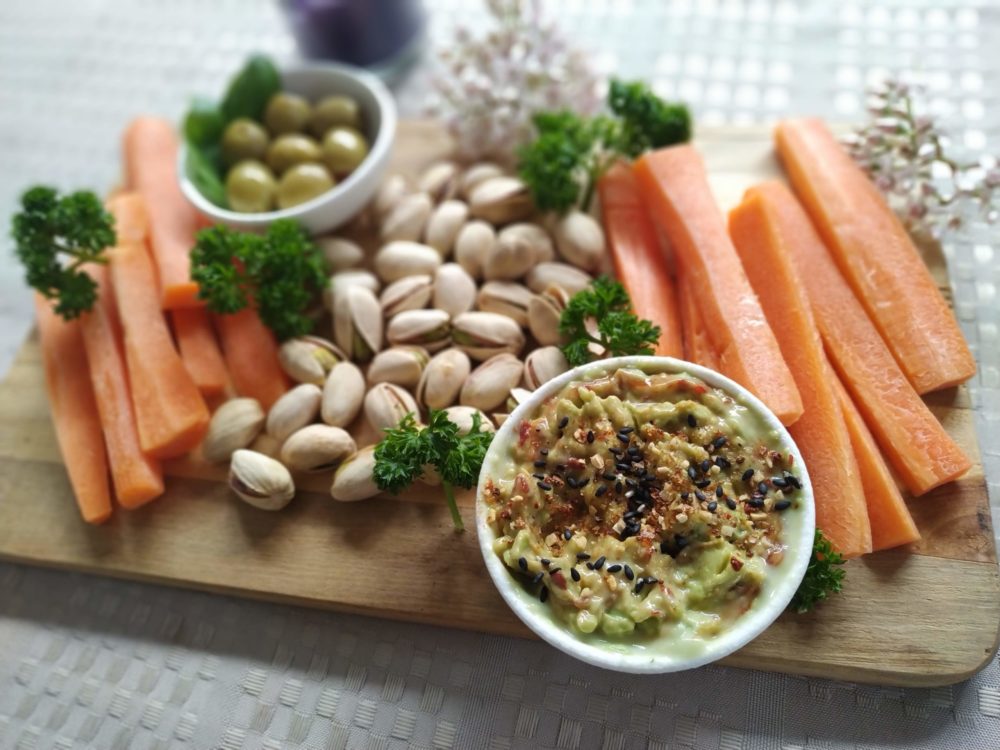 a wooden tray of vegetables and nuts with spiced avocado and white bean dip