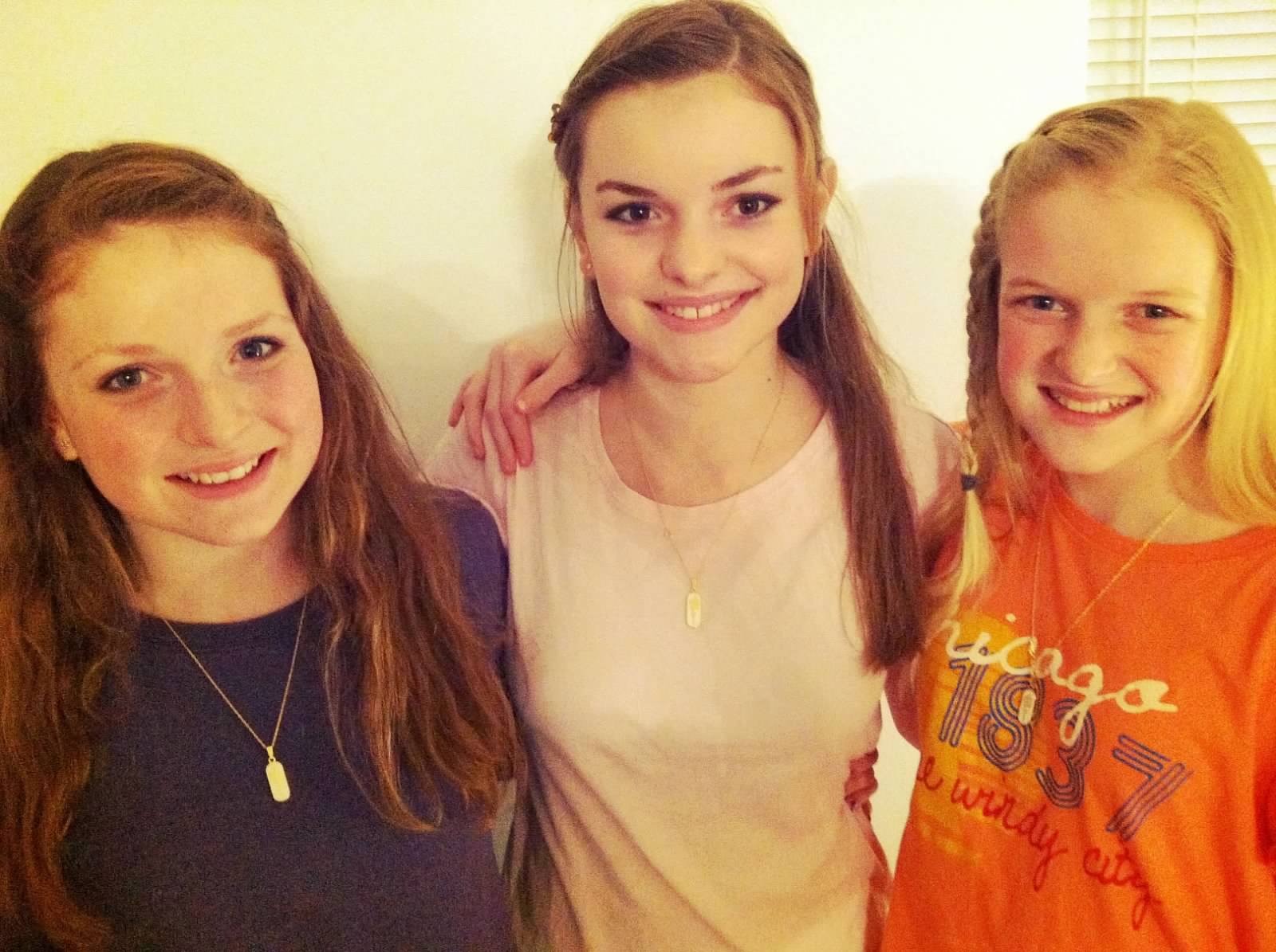 Three young girls wearing Mormon symbolic necklaces and smiling at the camera.