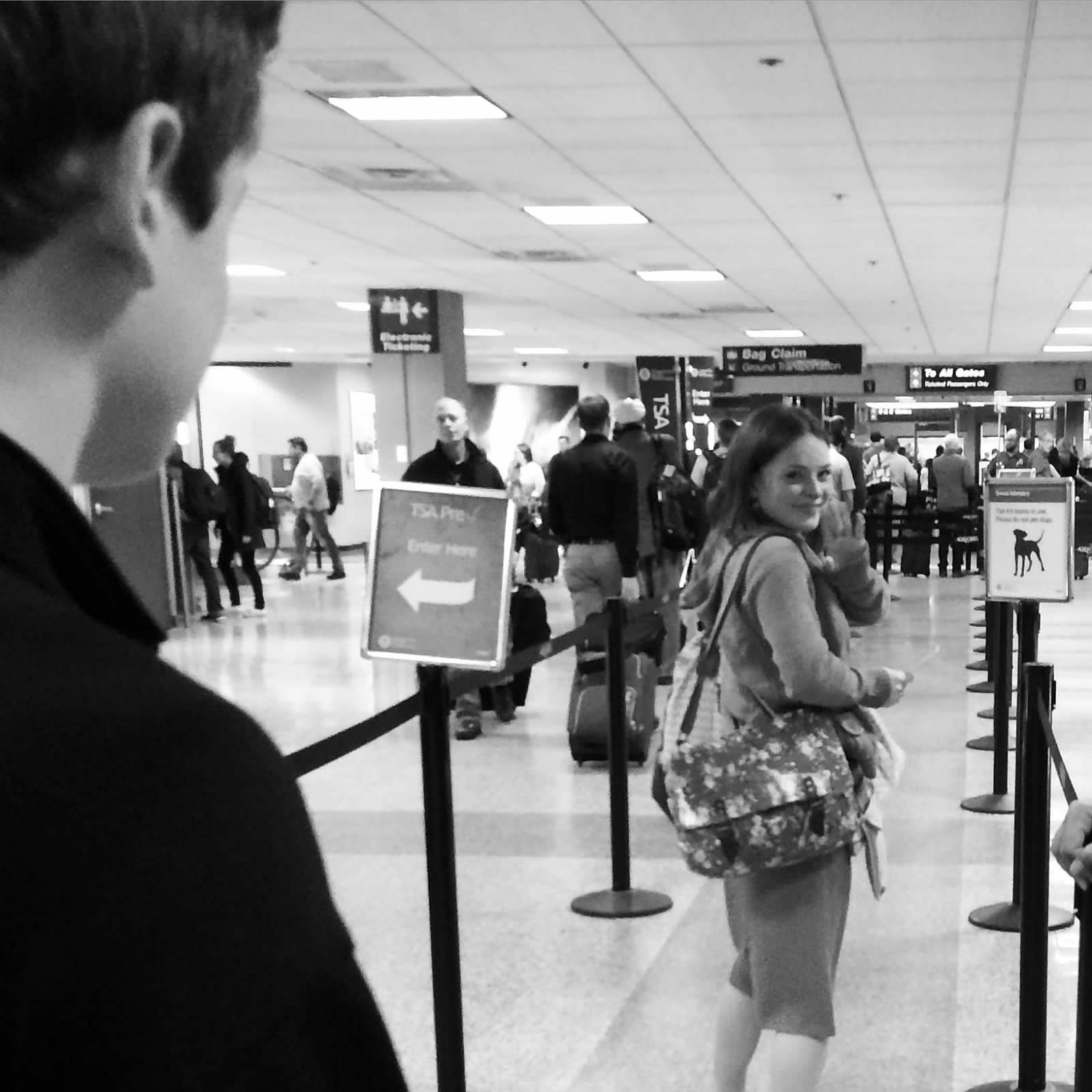 A girl is looking back at the camera and smiling as she enters the TSA line at the airport.