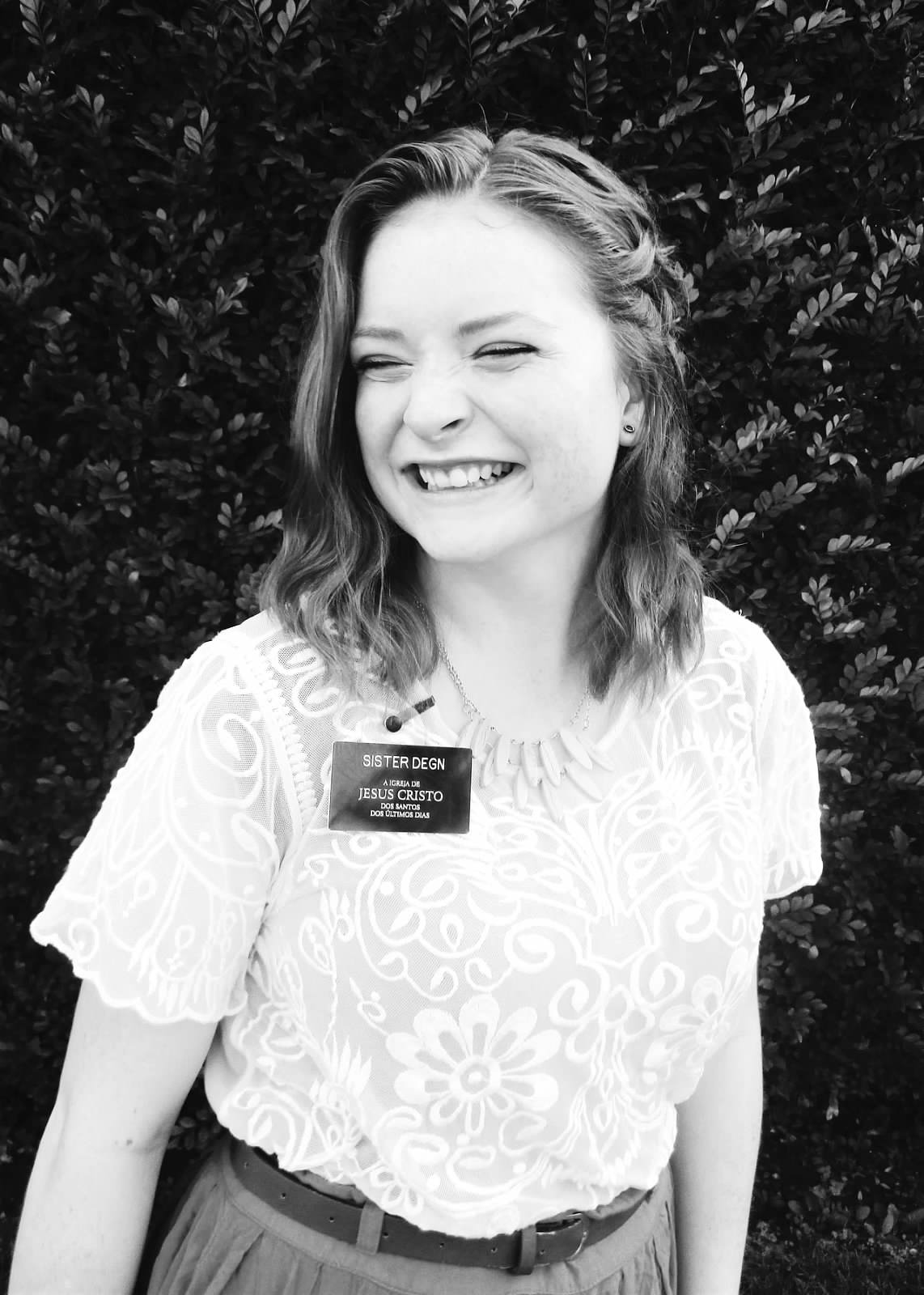 A black and white photo of a young woman, Emily Degn, wearing her Mormon name tag saying Sister Degn and smiling.