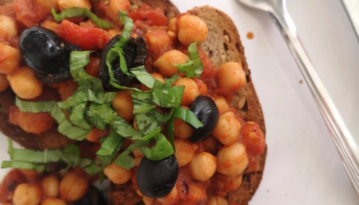 greek chickpeas on toast on a white plate with a fork
