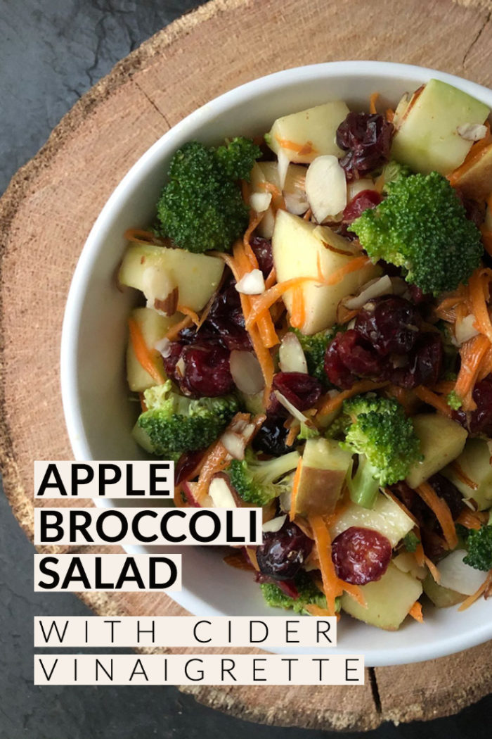 apple broccoli salad with cider vinaigrette in a white bowl against a brown and black background with overlayed caption
