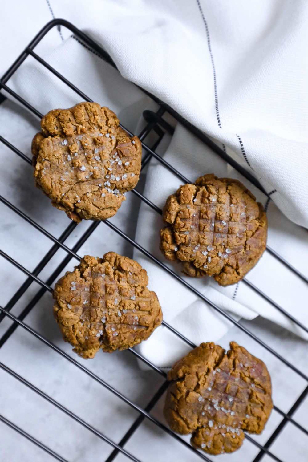 vegan peanut butter cookies on a wire cooling rack. a white tea towel is visible above.