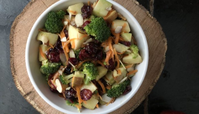 apple broccoli salad with cider vinaigrette in a white bowl against a brown and black background