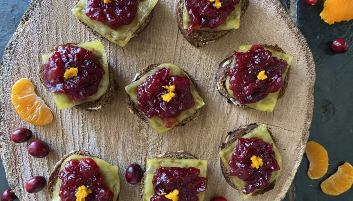 cranberry orange crostini with vegan cheese on a brown surface with a black background