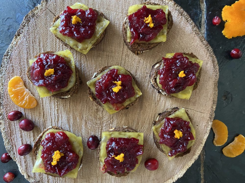 cranberry orange crostini with vegan cheese on a brown surface with a black background