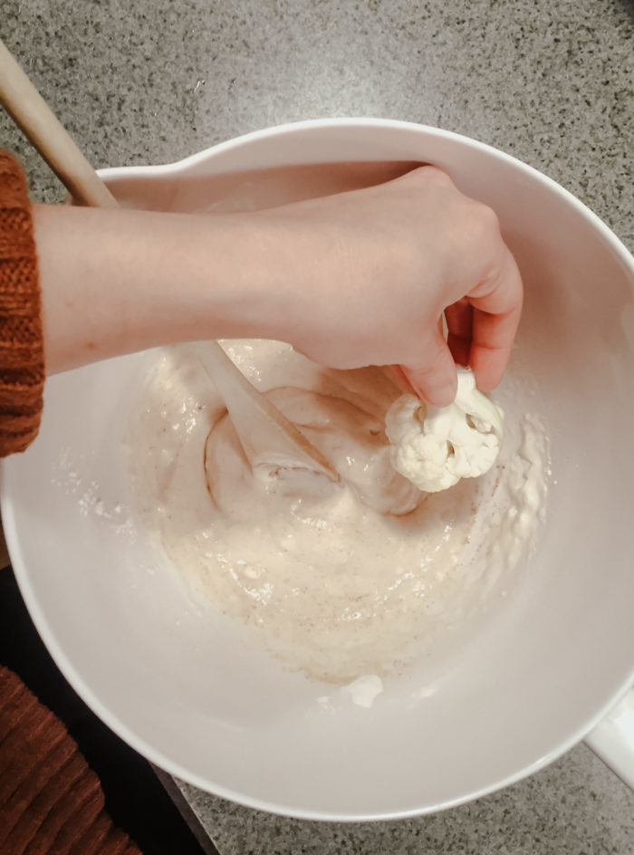 dipping a cauliflower floret in the batter
