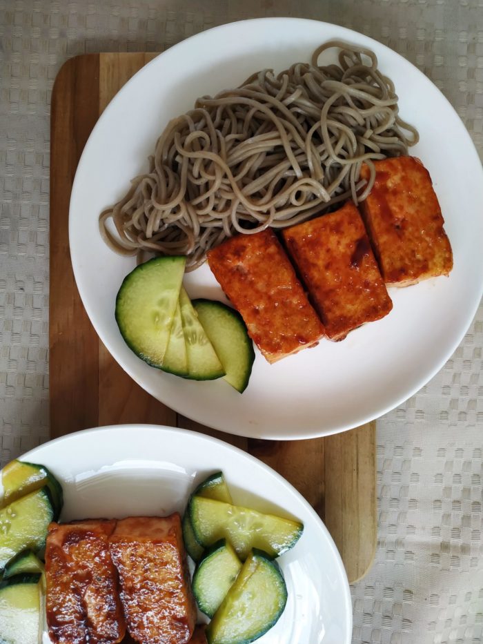 vegan bbq tofu with noodles on a white plate on a cutting board
