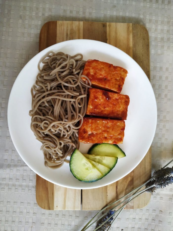 vegan bbq tofu with noodles on a white plate on a cutting board