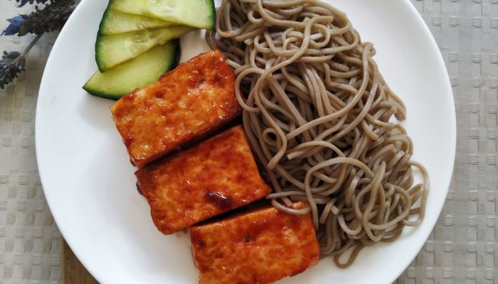 vegan bbq tofu with noodles on a white plate on a cutting board