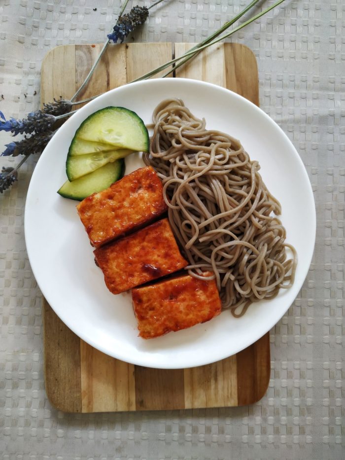 vegan bbq tofu with noodles on a white plate on a cutting board