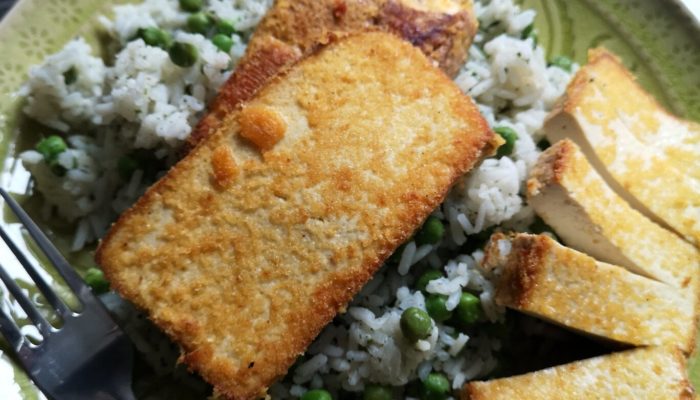 tofu schnitzel with rice and peas on a green plate with a fork