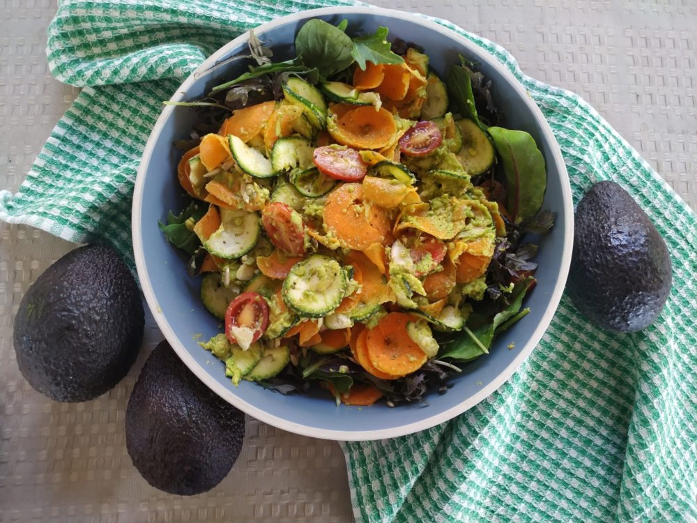 vegan south east asian rainbow salad with creamy peanut avocado sriracha dressing in a bowl next to avocados