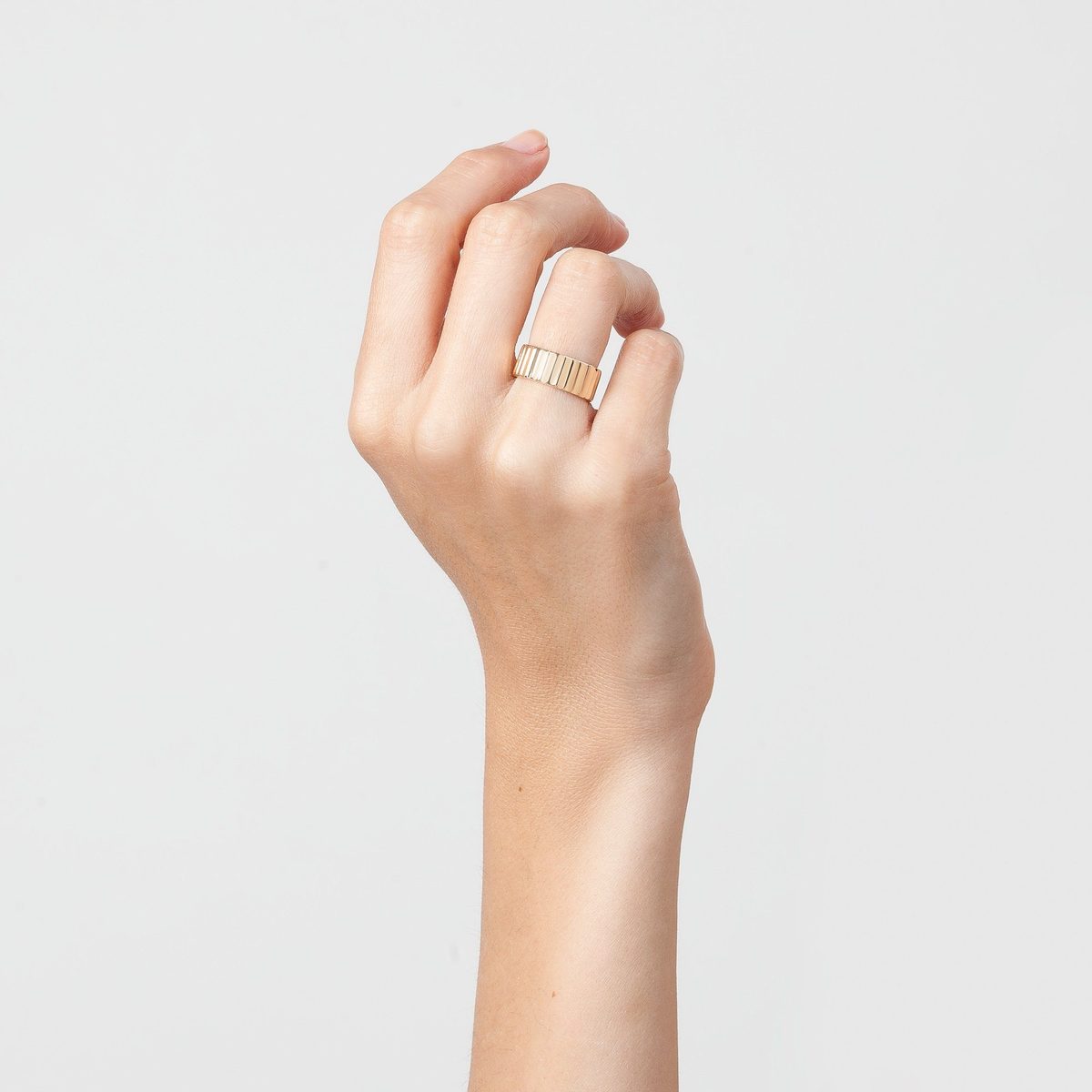 a hand wearing a recycled gold infinity ring against a white background