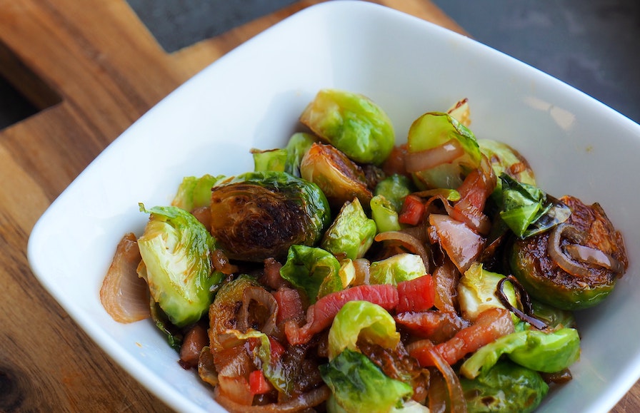 thai-inspired brussels sprouts in a white dish on a wooden cutting board.