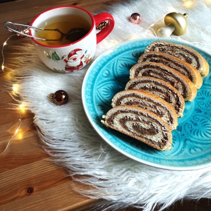 vegan bejgli; hungarian walnut roll on a blue plate with a cup of tea