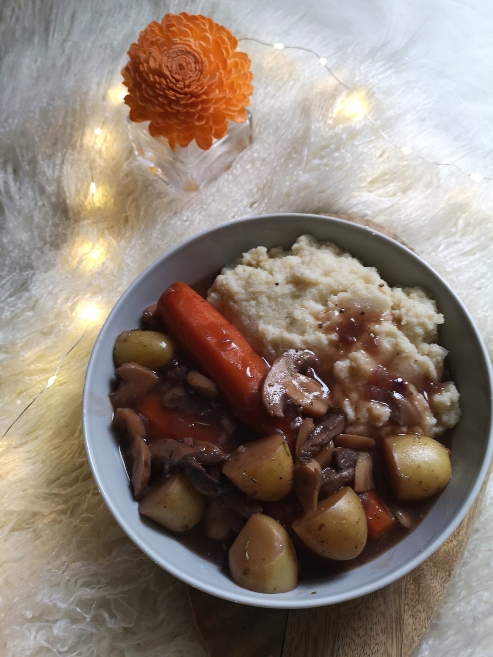 vegan coq au vin against a white background with lights and a flower