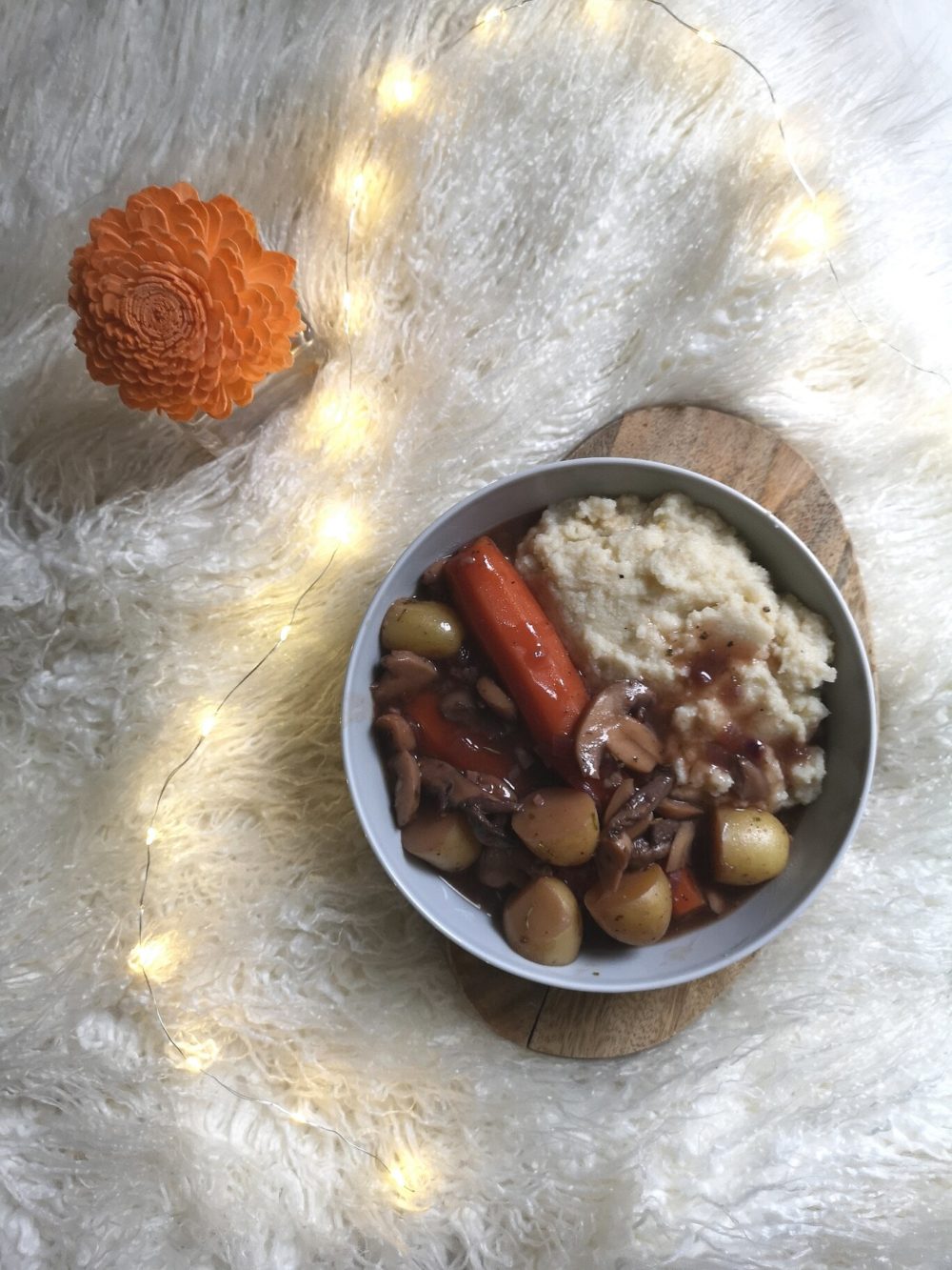vegan coq au vin against a white background with lights and a flower