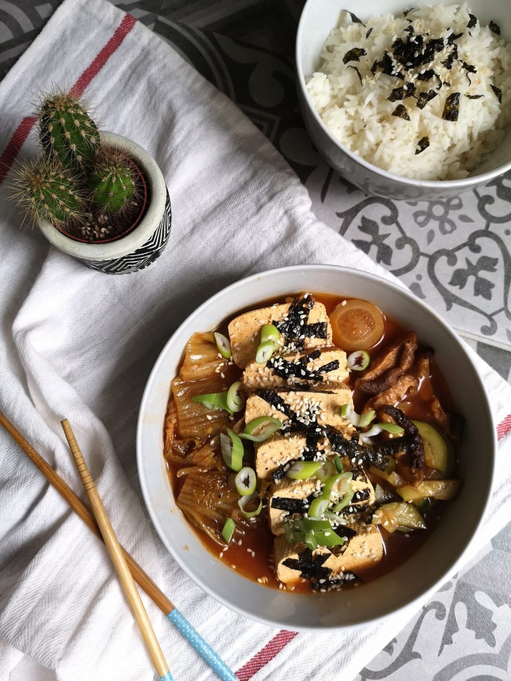 vegan kimchi jigae next to a cactus and bowl of rice