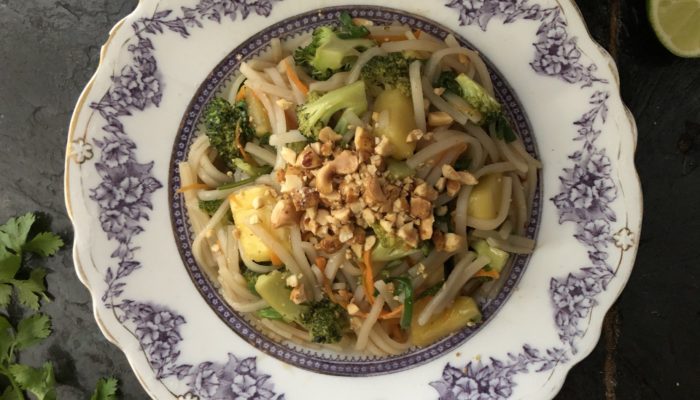 vegan pineapple pad thai on a floral plate with a dark background