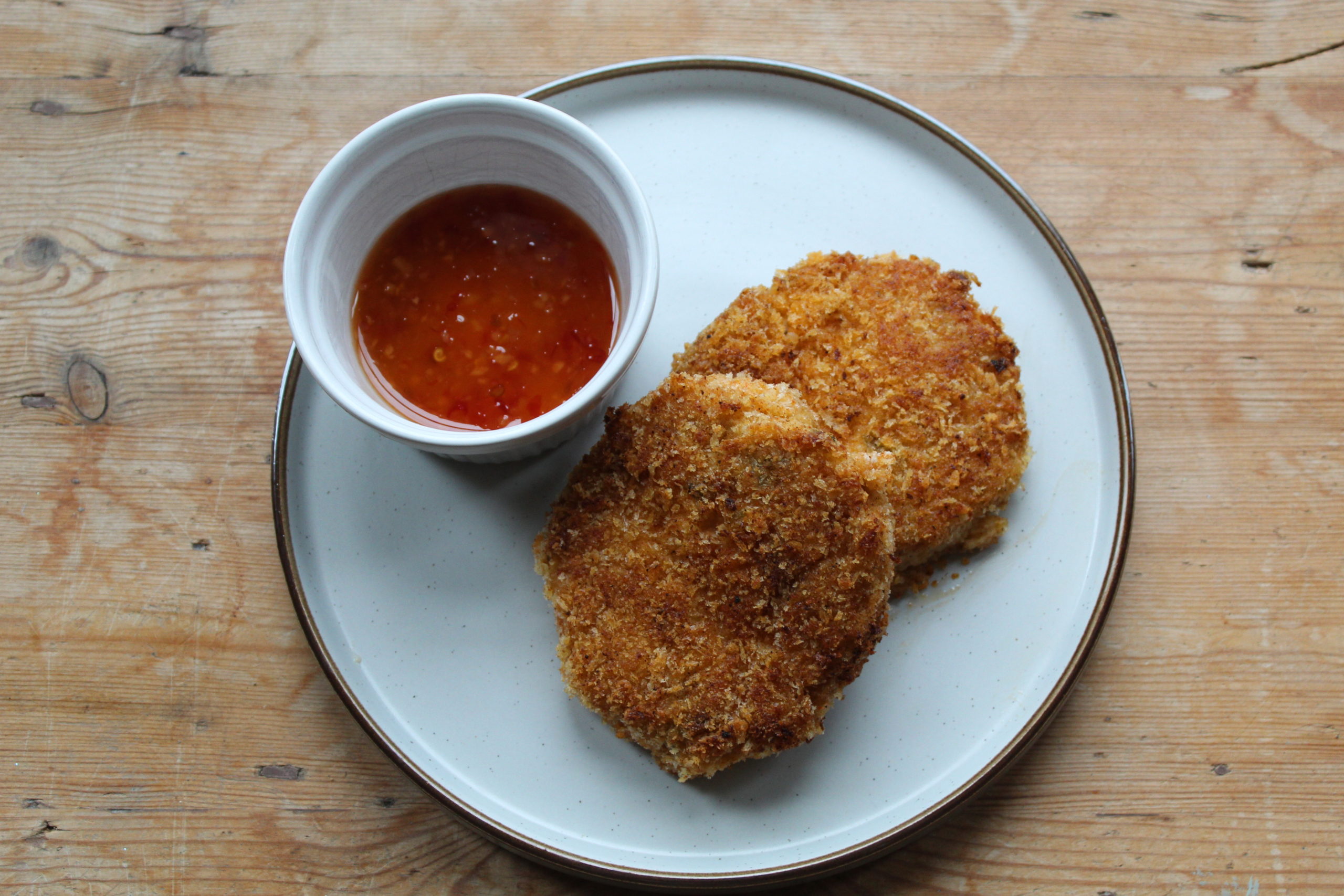 vegan fish cakes on a white plate with dipping sauce against a wooden table