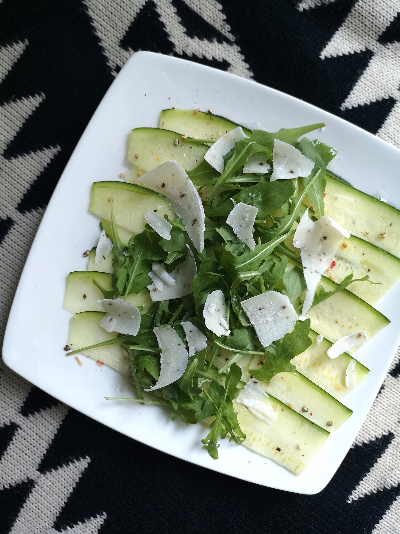 zucchini carpaccio salad with vegan truffle cheese on a white plate