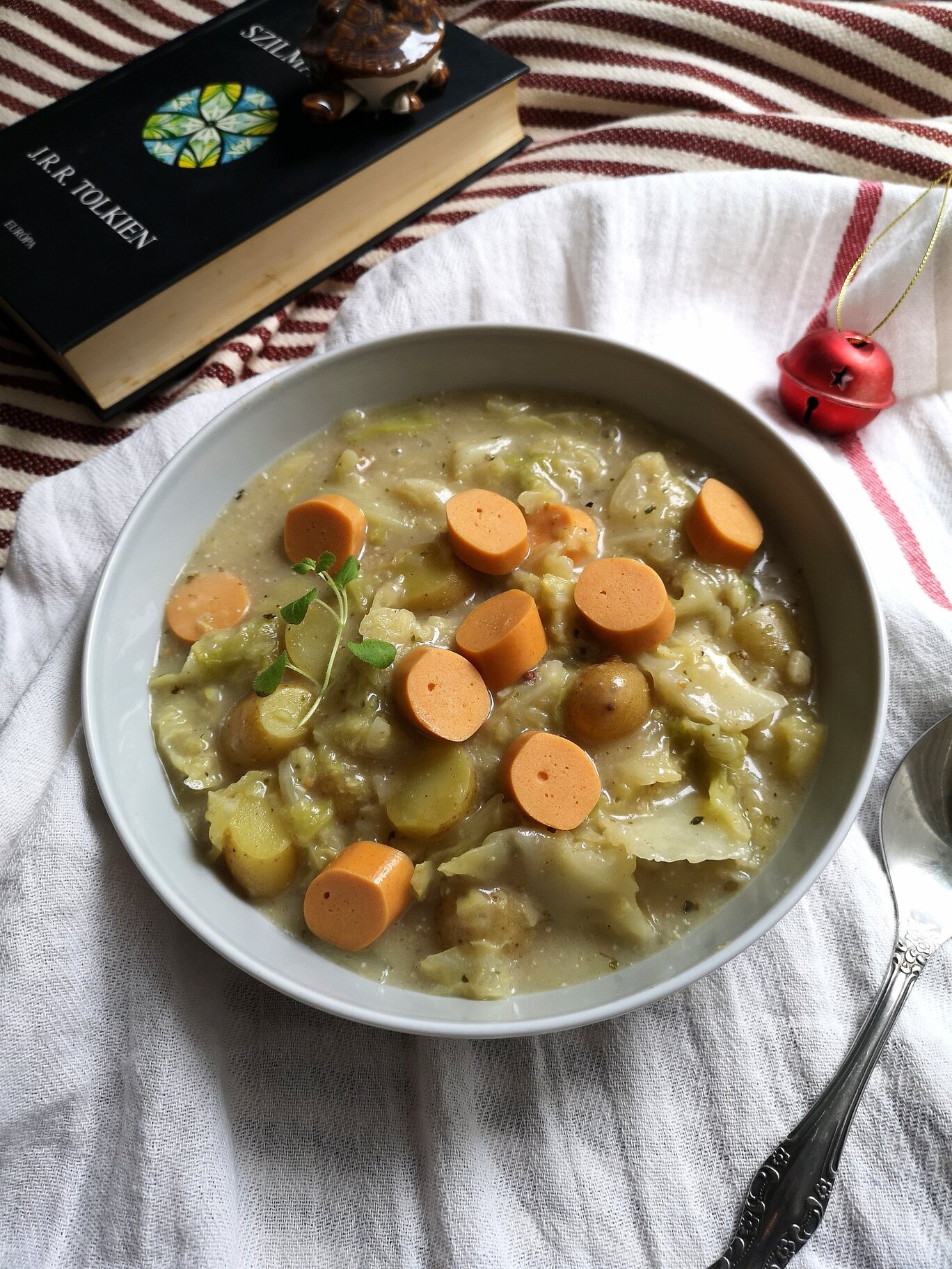 vegan frankfurter soup in a white bowl next to a spoon and a book