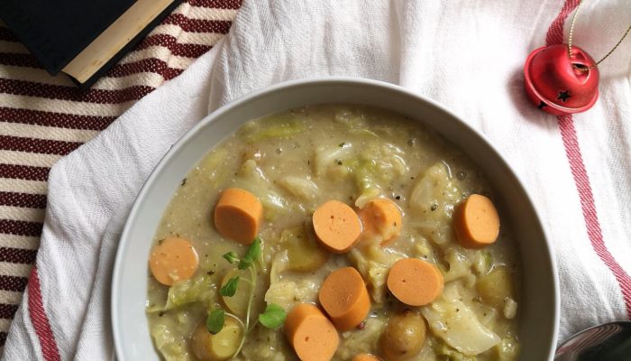 vegan frankfurter soup in a white bowl next to a spoon