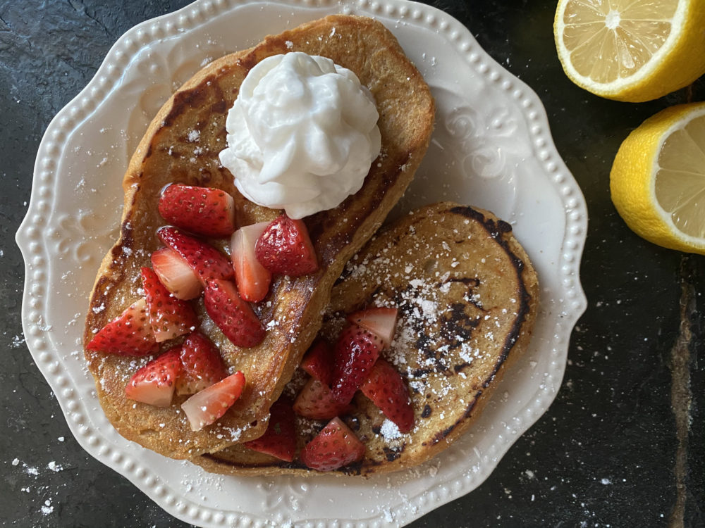 vegan french toast on a white plate against a black background with lemons
