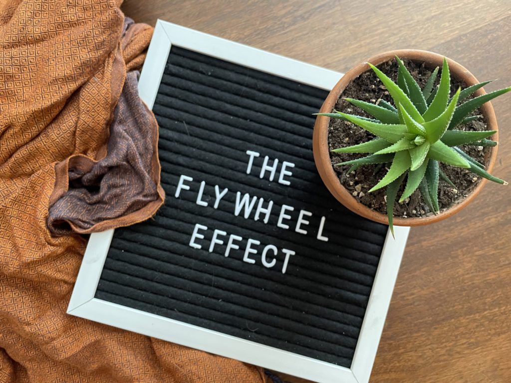 letter board reading "The Flywheel Effect" next to a scarf and succulent