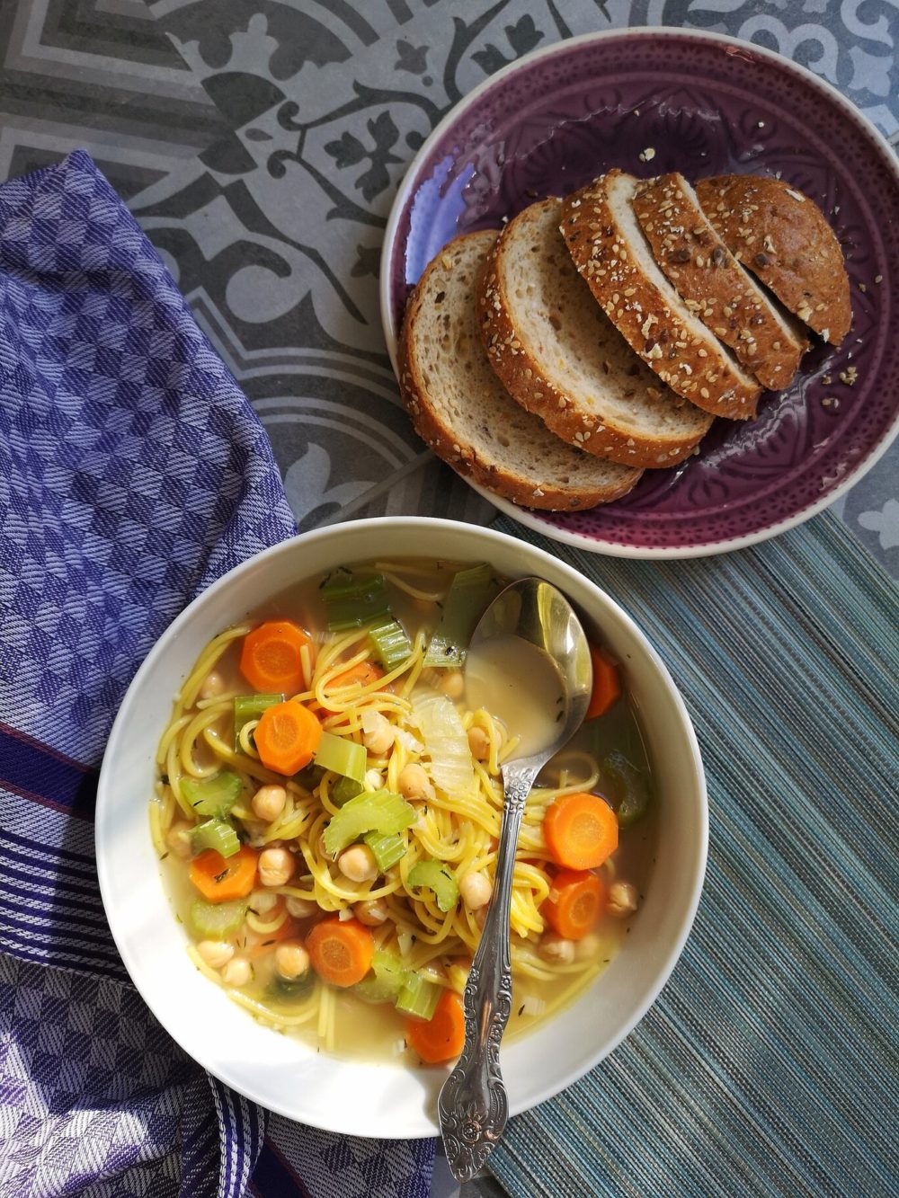 vegan chickpea spaghetti soup in a bowl with a spoon next to bread slices on a plate