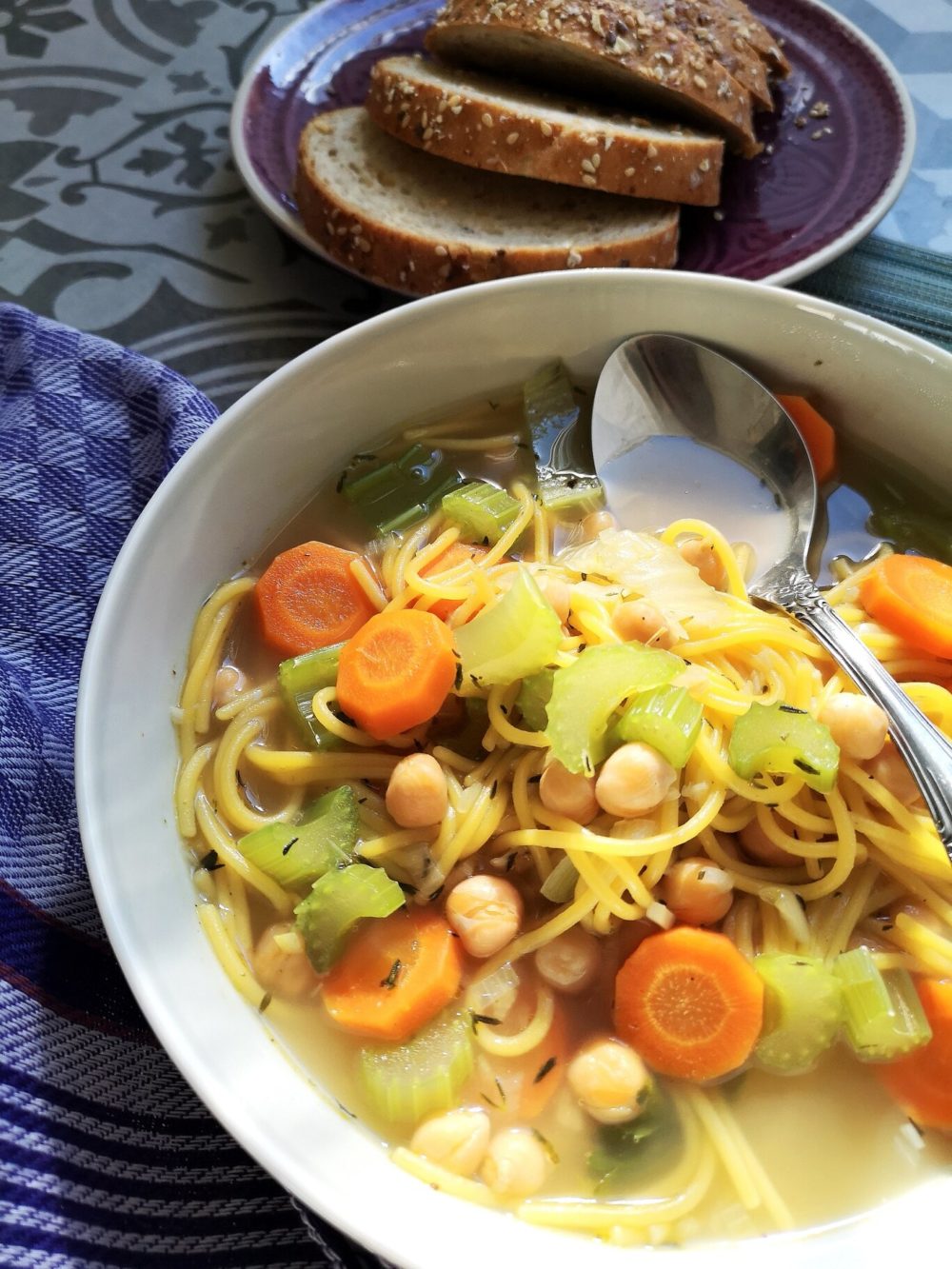 vegan chickpea spaghetti soup in a bowl with a spoon next to bread slices on a plate