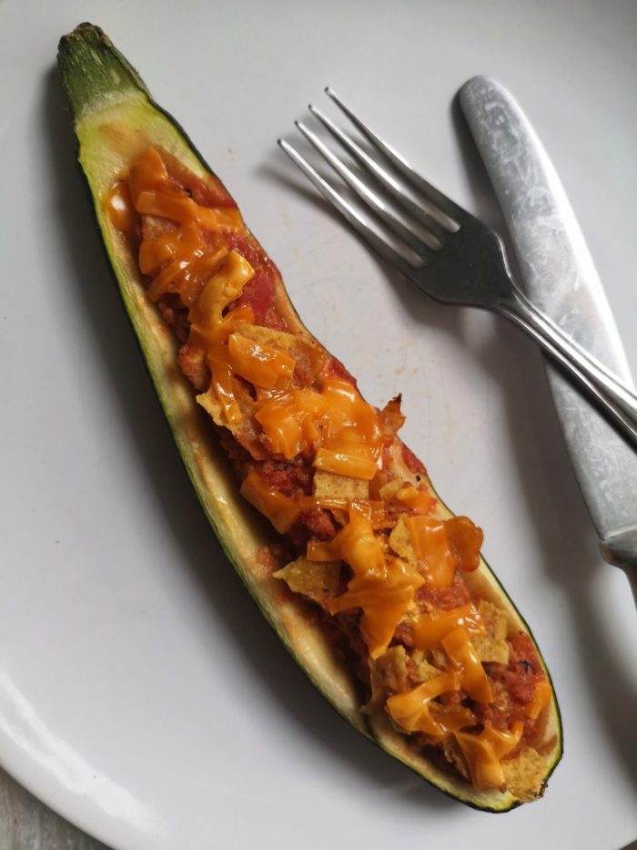 vegan nacho stuffed zucchini boat on a white plate with a fork and knife