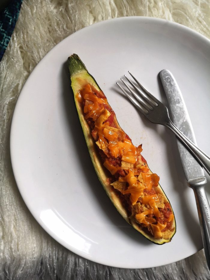 vegan nacho stuffed zucchini boat on a white plate with a fork and knife