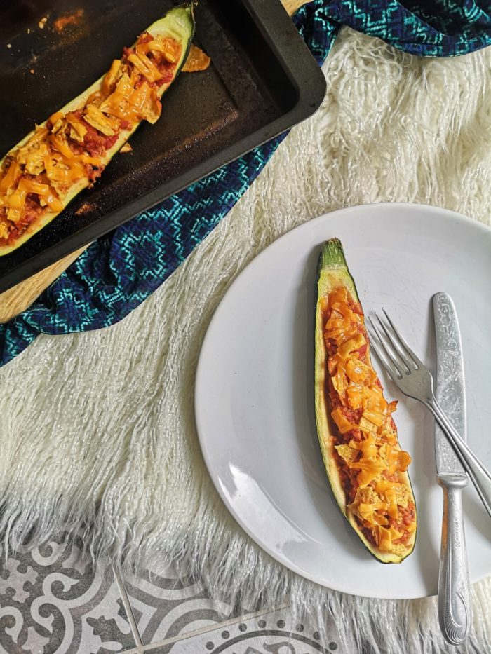 vegan nacho stuffed zucchini boat on a white plate with a fork and knife
