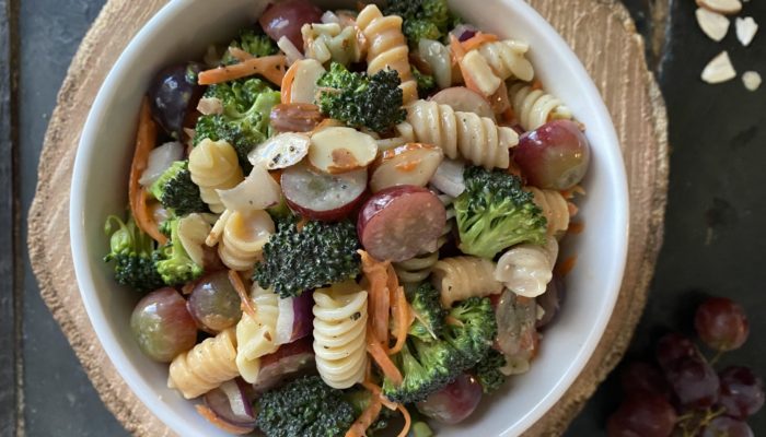 broccoli pasta salad in a white dish with a brown and black background