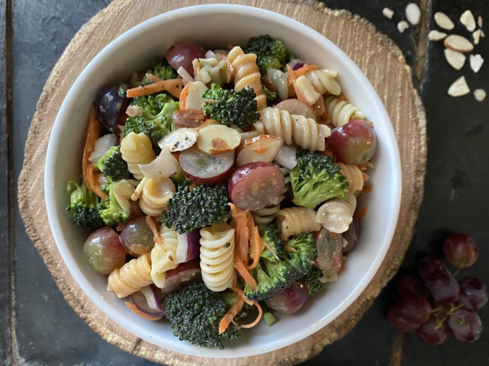 broccoli pasta salad in a white dish with a brown and black background